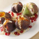 Fresh figs stuffed with mizithra sheep's cheese and toasted almond slivers, topped with honey and garnished with pomegranate seeds, seen from above.