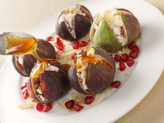 Fresh figs stuffed with mizithra sheep's cheese and toasted almond slivers, topped with honey and garnished with pomegranate seeds, seen from above.