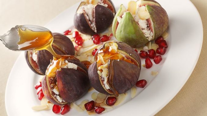 Fresh figs stuffed with mizithra sheep's cheese and toasted almond slivers, topped with honey and garnished with pomegranate seeds, seen from above.