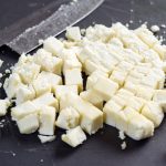 Freshly cut paneer cheese on a cutting board with knife in the background. shallow focus across the middle.