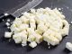 Freshly cut paneer cheese on a cutting board with knife in the background. shallow focus across the middle.