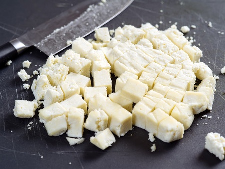 Freshly cut paneer cheese on a cutting board with knife in the background. shallow focus across the middle.