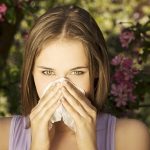 Young woman with allergy during sunny day is wiping her nose.