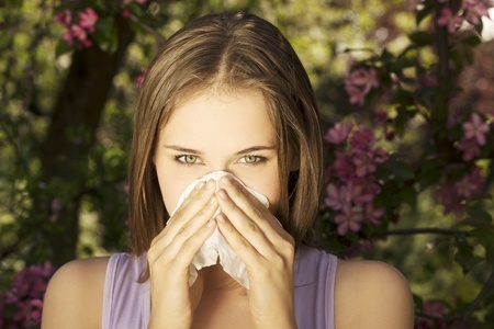 Young woman with allergy during sunny day is wiping her nose.