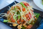 green papaya salad in black plate on table background