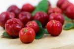 Acerola cherries laid out on a table in both full focus shot with some green leaves.