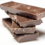 Chunks of dark chocolate piled up on a white background. An example of confectionary.