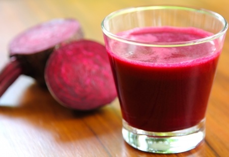 Beetroot juice in a conical glass with cut beetroot on a wooden table.