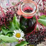 Elderberry juice in a Kilner jar surrounded by elderberries, green leaves and a daisy.