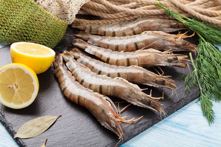 fresh raw tiger prawns and fishing equipment on wooden table