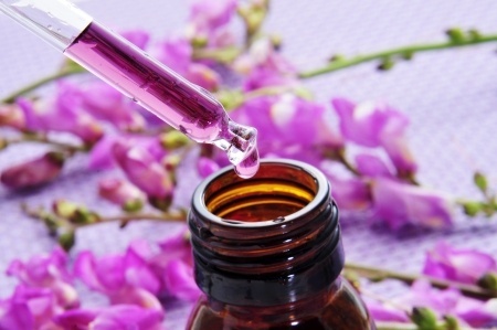 Close up of a dropper bottle and a pile of purple flowers on a purple background