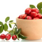 Ripe hip roses with leaves in cup, isolated on white background.