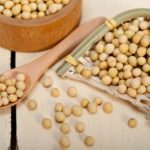 organic soya beans displayed on a wooden table with a spoon, bowl and other strange container.