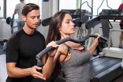 Woman exercising with weights and being spotted by male helper.