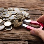 Businessman's Hand Pulling Coins With Magnet On Wooden Table. magnetic immobilisation