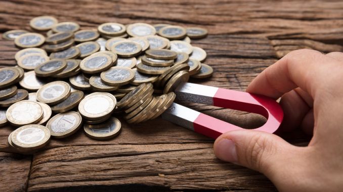Businessman's Hand Pulling Coins With Magnet On Wooden Table. magnetic immobilisation