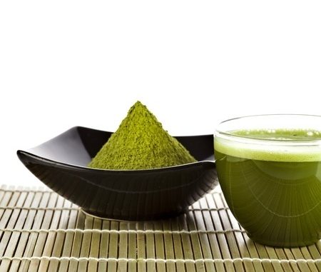 Green tea in a black bowl with a clear glass cup of the beverage next to it.