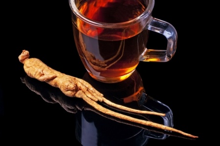 Ginseng tea on a black background with a root of ginseng.