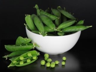 Peas in pods and in a white bowl on a dark grey background.