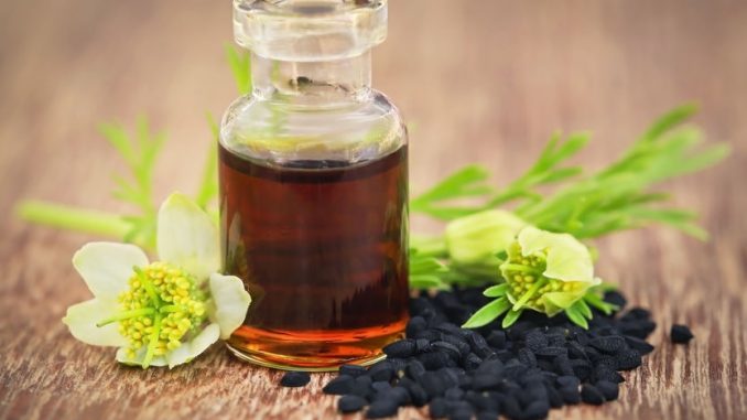 Nigella flower with seeds and essential oil in a glass bottle