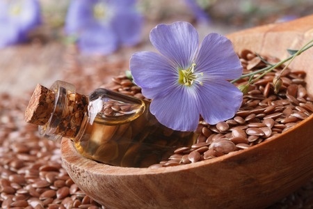 Flax oil in a glass bottle, flowers and seeds in a wooden spoon macro.