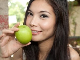 Beautiful girl about to chomp on a green apple.