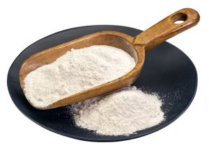 Cassava (yuca) flour on a wooden scoop and plate. It is a gluten free and grain free replacement for wheat flour.
