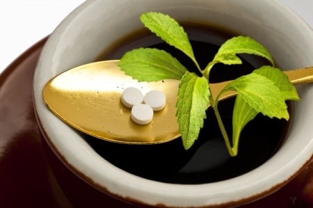 Stevia pills and stevia plant on a golden spoon in a bowl.