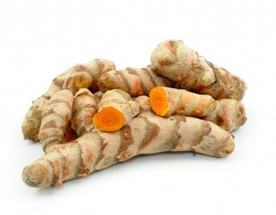 Turmeric rhizomes, some cut in half to show their orange colour on a white background.