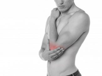 Naked man showing inflammation in his elbow as he holds it against his naked torso.