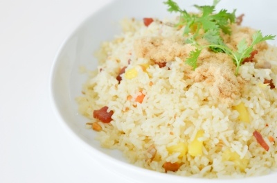 A mixed vegetable rice dish with a sprg of green herb on top, in a white bowl on a white background.