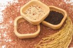 Three bowls containing different coloured rice. The photo is taken from the top and the bowls are resting on a bed of red rice with a rice 'sheath' .