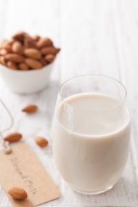 Almond milk in a glass, with almonds in a bowl.