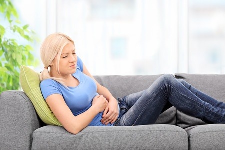 A blonde woman clutching her stomach and suffering food poisoning from something like botulism.