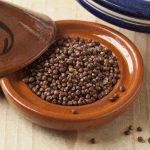 Alligator pepper or maniquette pepper or maleguetta pepper in a brown tagine bowl on a wooden table.