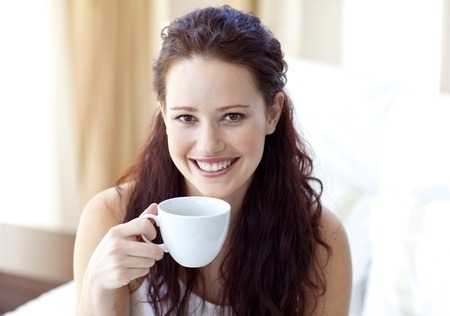 Beautiful girl, smiling, looking face on, holding a white cup of coffee