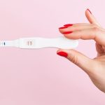 41890595 - beautiful female hand with red fingernails holding positive pregnancy test isolated on pink background. motherhood, pregnancy, birth control concept. minimal sparse modern image language.