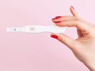 41890595 - beautiful female hand with red fingernails holding positive pregnancy test isolated on pink background. motherhood, pregnancy, birth control concept. minimal sparse modern image language.
