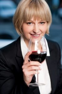 An attractive woman in a smart suit drinking a large glass of red wine from a good sized wine glass. Courtesy of FreeDigitalPhotos.net
