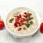Oat porridge with healthy goji and squash seeds on white wooden table