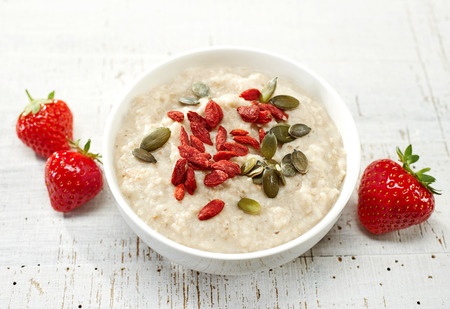 Oat porridge with healthy goji and squash seeds on white wooden table