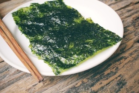 Seaweed on a white plate with chopsticks, all on a wooden table.