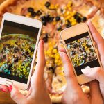 female friends using smartphones to take photos of their pizza