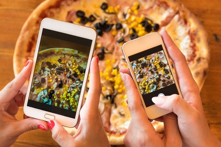 female friends using smartphones to take photos of their pizza