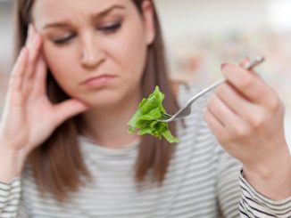 Displeased young woman eating green leaf lettuce. shallow depth of field, focus on foreground