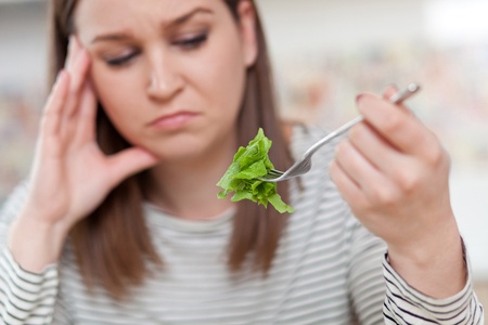 Displeased young woman eating green leaf lettuce. shallow depth of field, focus on foreground