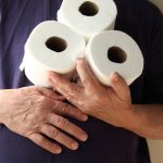 Man with hand over his stomach holds three rolls of toilet paper. A symptom of gastroenteritis and inflammatory bowel disease.