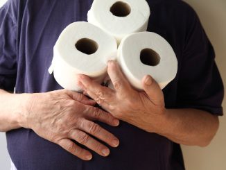 Man with hand over his stomach holds three rolls of toilet paper. A symptom of gastroenteritis and inflammatory bowel disease.