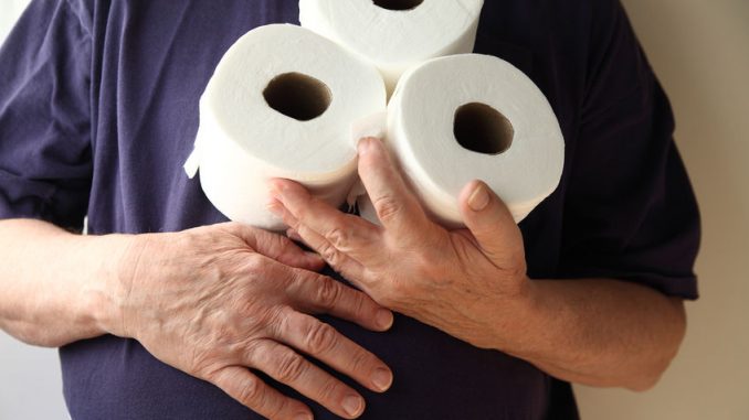 Man with hand over his stomach holds three rolls of toilet paper. A symptom of gastroenteritis and inflammatory bowel disease.