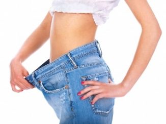 Woman showing how much weight she has lost from her stomach, wearing blue jeans.
